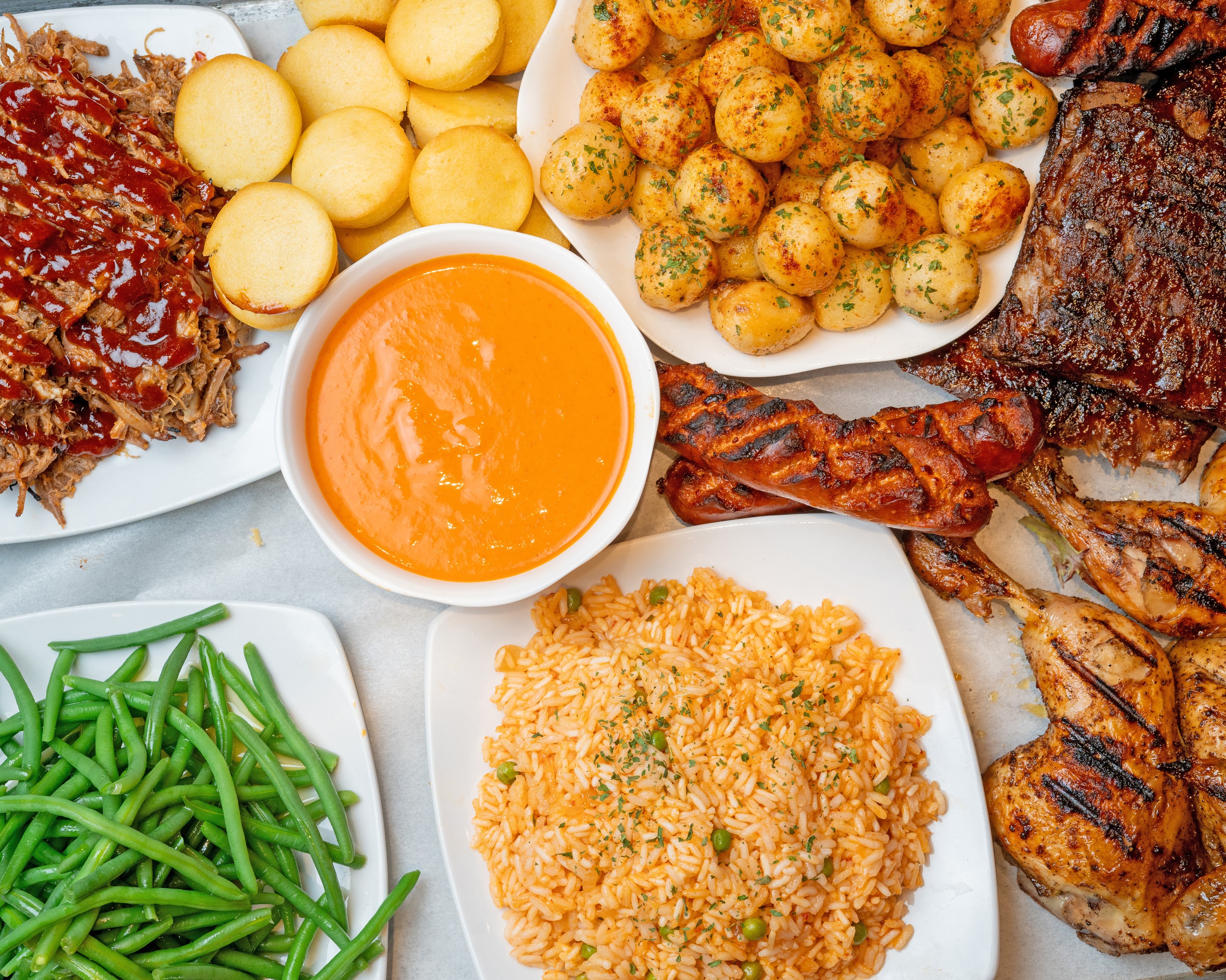 An abundant BRAVA family feast: whole fire-grilled chicken, BBQ ribs, signature roasted potatoes, BRAVA rice, fresh salads, house-made sauces and fresh buns